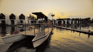 A boat docked at a waterfront property with multiple overwater bungalows, a dock, and calm water reflecting the sunset. - Port Ville Resort (Kampot)