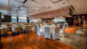 A spacious dining area with multiple tables and chairs, a kitchen in the background, and large windows providing natural light. - Gleetour Hotel Guizhou  (Qiandongnan)