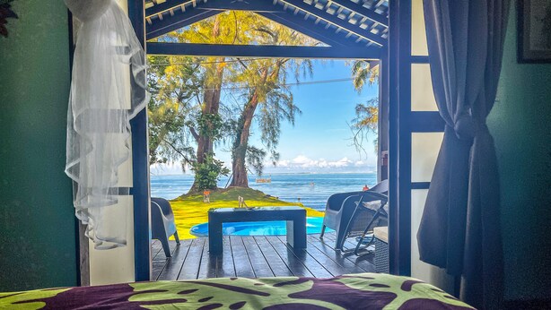 A room with a bed, a small table, and a view of the ocean. - Teahupoo: beachfront, the lagoon and the wave, at the foot of the mountains ! (teahupoo)