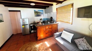 A compact living space with a kitchenette, a sofa, and a patterned rug. - Teahupoo: beachfront, the lagoon and the wave, at the foot of the mountains ! (teahupoo)