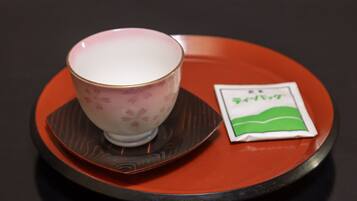 A teapot with a floral pattern on a saucer, placed on a red tray with a packet of tea beside it.