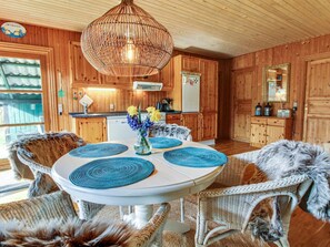 Cozy cabin-style kitchen with wooden cabinetry, a vintage refrigerator, and a dining area with wicker chairs and a pendant light.