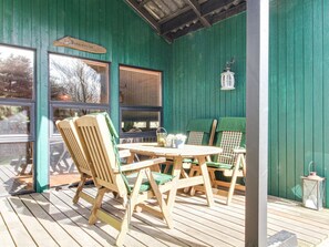 Relax in the serene outdoor seating area with a wooden deck and a green-painted wall, featuring a round table and two comfortable chairs.