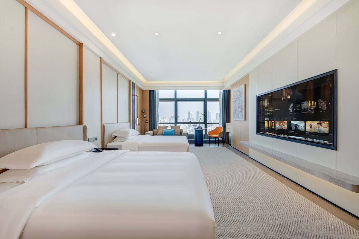 Quarto de hotel com três camas, uma TV grande e vista para a cidade.