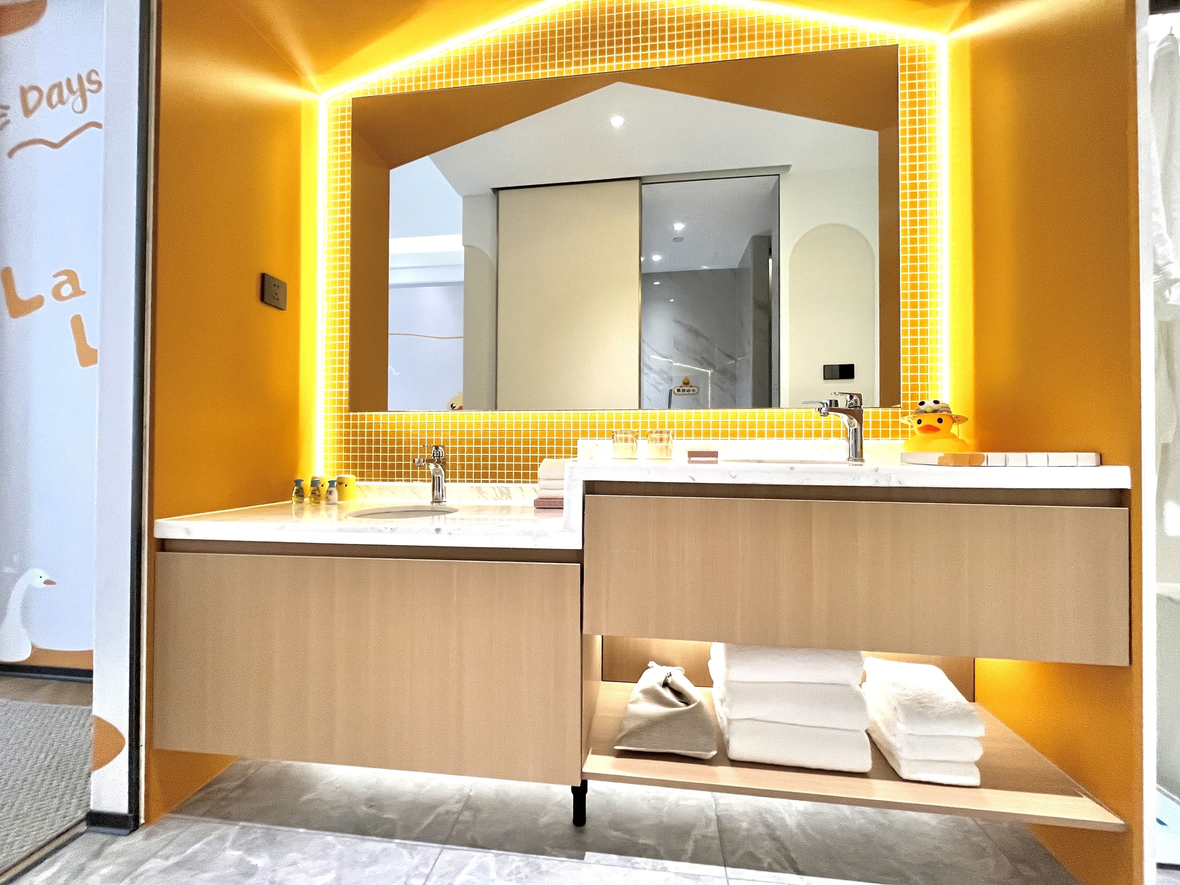 Un bagno moderno con uno specchio grande, un lavabo e un mobile contenitore. Asciugamani e articoli da toilette sul ripiano.