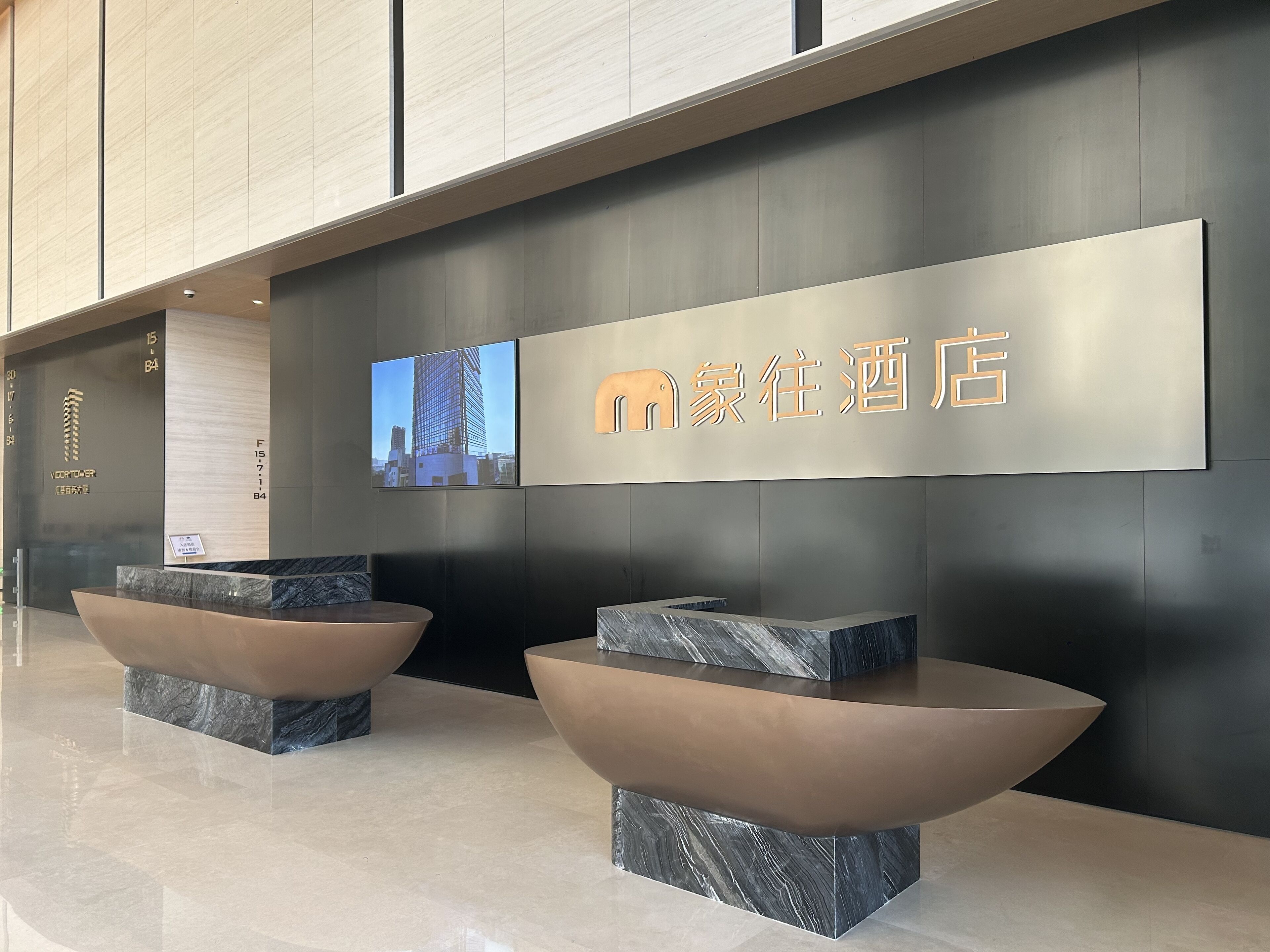 A modern hotel reception area with a digital screen displaying a cityscape, a reception desk, and a large sign with the hotel name.