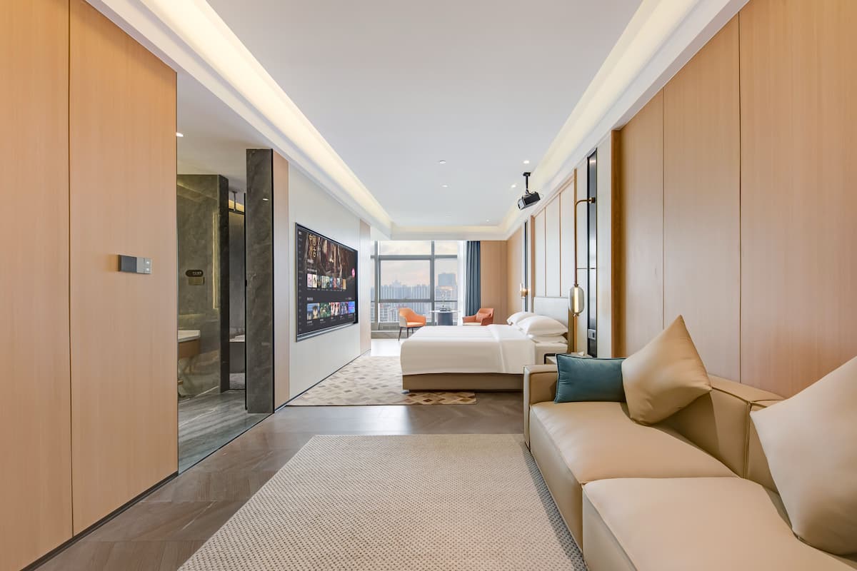 Quarto de hotel moderno com uma cama grande, um sofá, uma TV e vista para a cidade.