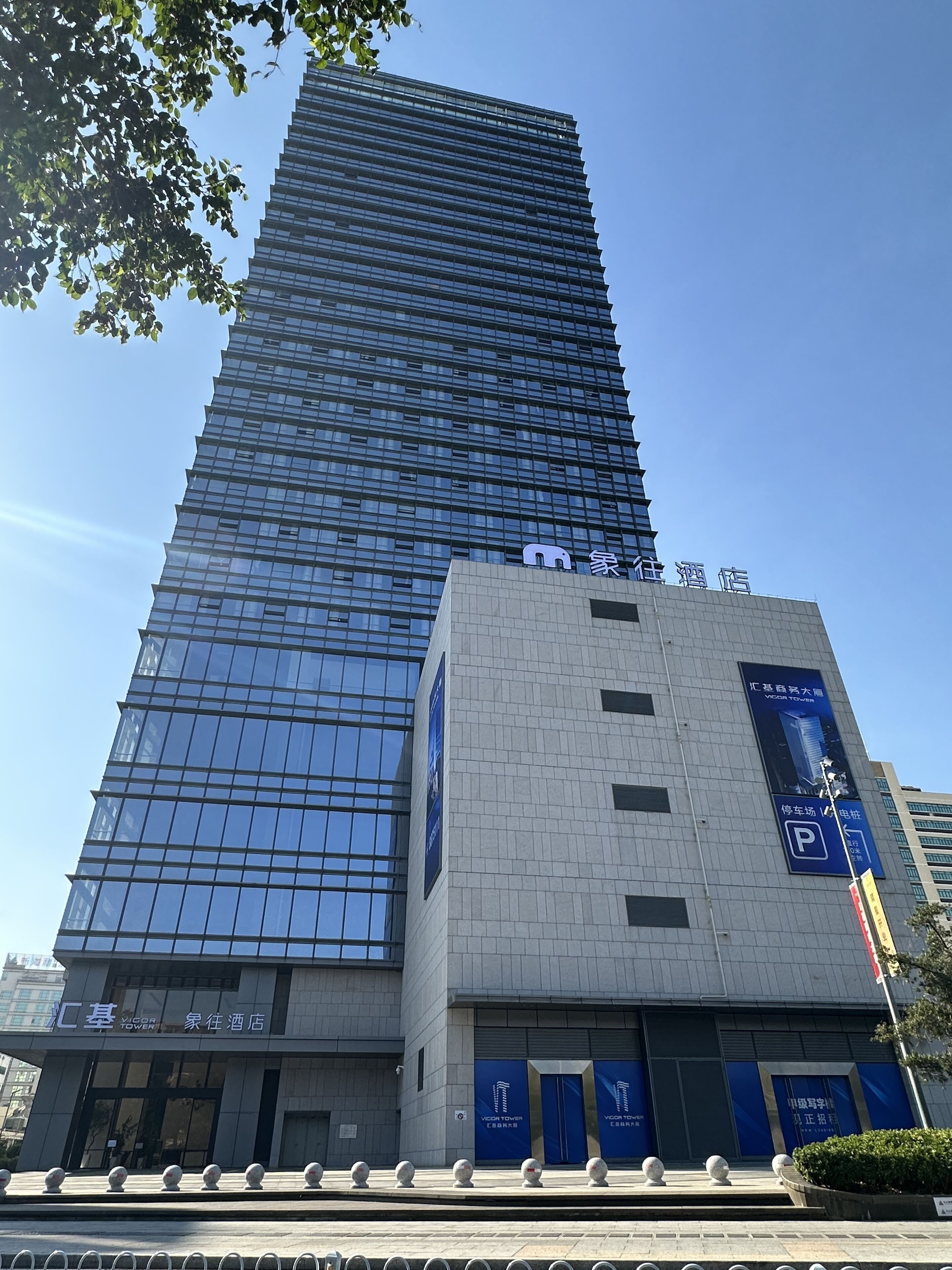 Ein hohes, modernes Gebäude mit Glasfassade und ein kleinerer, daran angrenzender Bau mit Beschilderung.