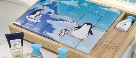 A wooden tray with a penguin-themed shaving kit, a mineral body lotion, and two bottles of bath products.