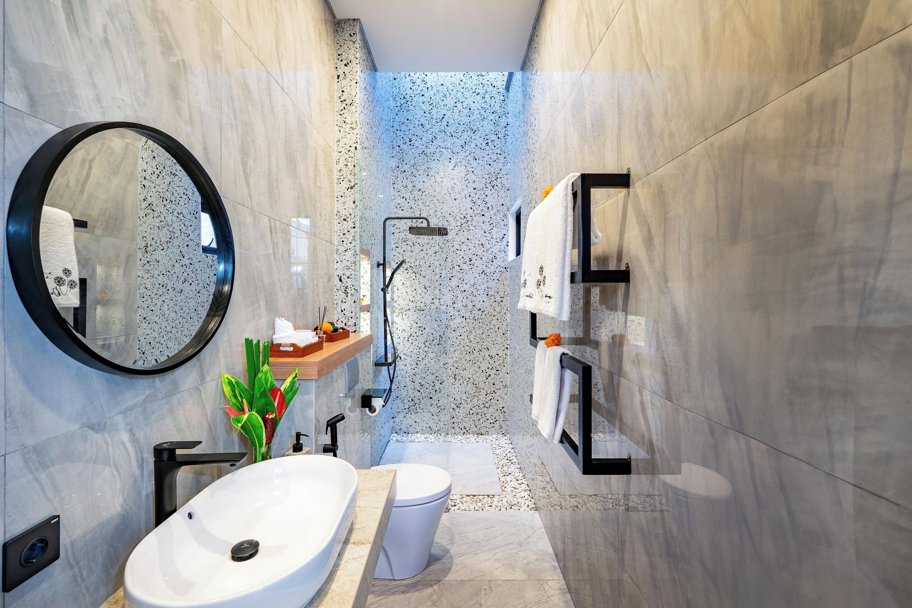 A modern bathroom with a round mirror, a white sink, a toilet, and a shower area.