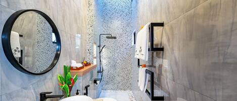 A modern bathroom with a round mirror, a white sink, a toilet, and a shower area.