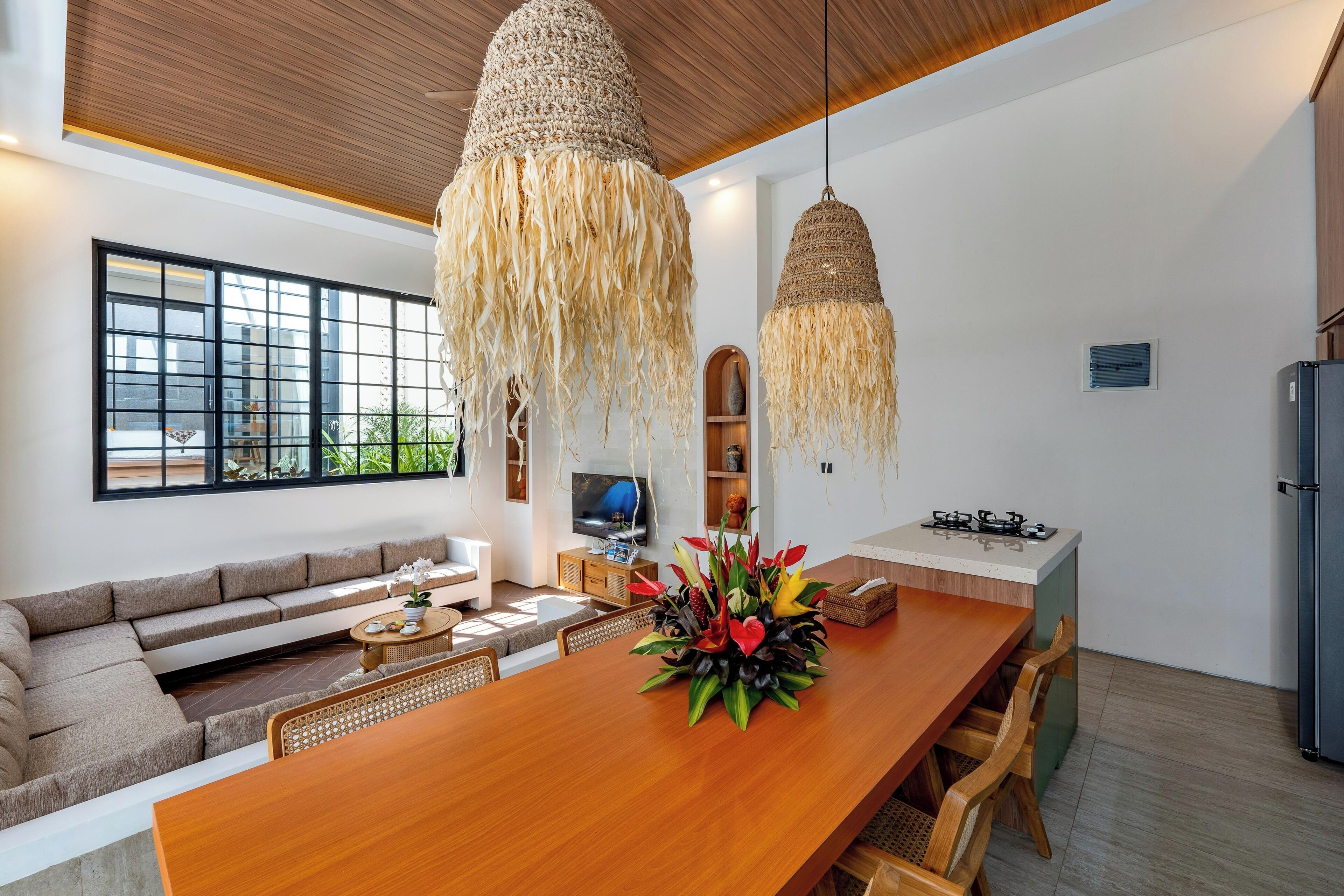 Een moderne woonkamer met een houten eettafel, een bank en een keuken met een koelkast en fornuis.