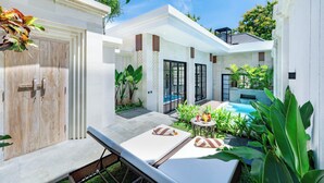 Un espace piscine extérieur moderne, doté de chaises longues, d’une petite table avec des fruits et d’une végétation luxuriante.