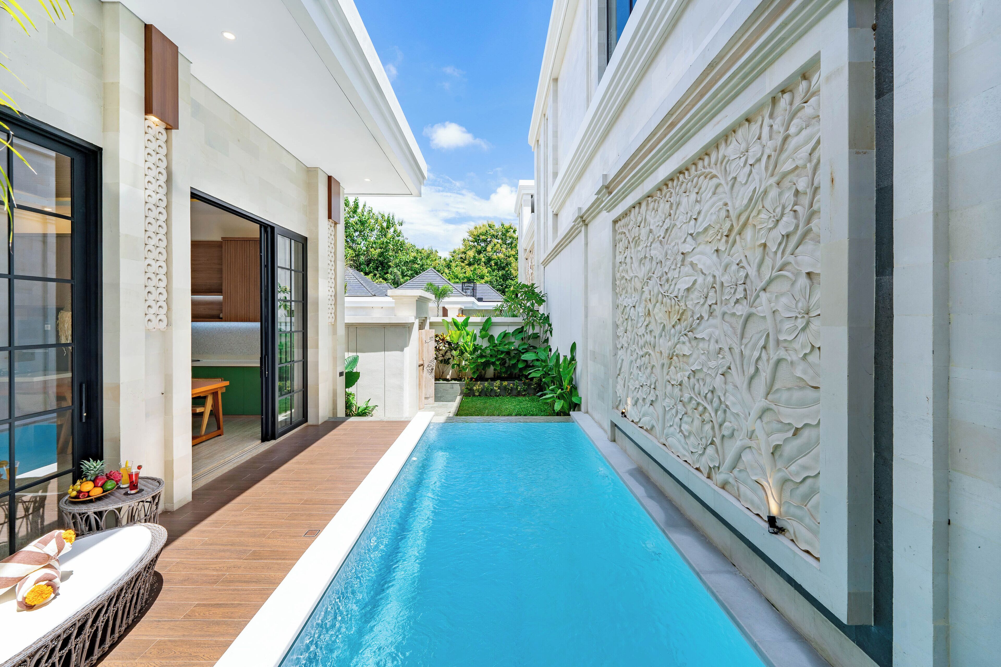 A swimming pool with a wooden deck, a glass door entrance, and a decorative wall.
