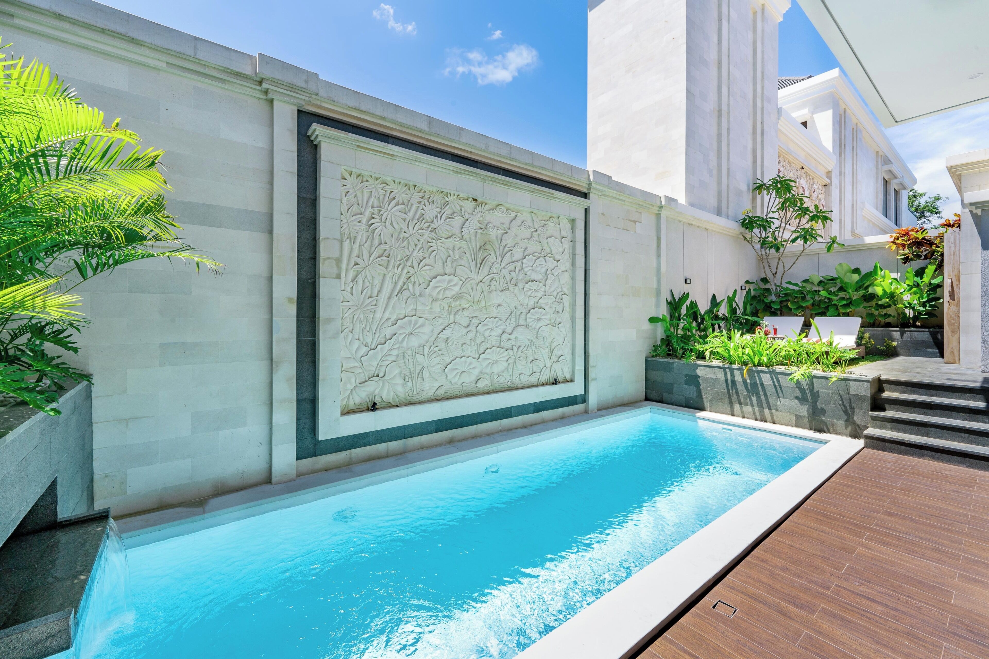 A swimming pool with a stone wall and a wooden deck.