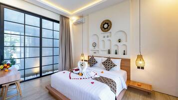 A modern hotel room with a large window, a bed with a decorative swan centerpiece, a small table with fruit, and a wall-mounted light fixture.