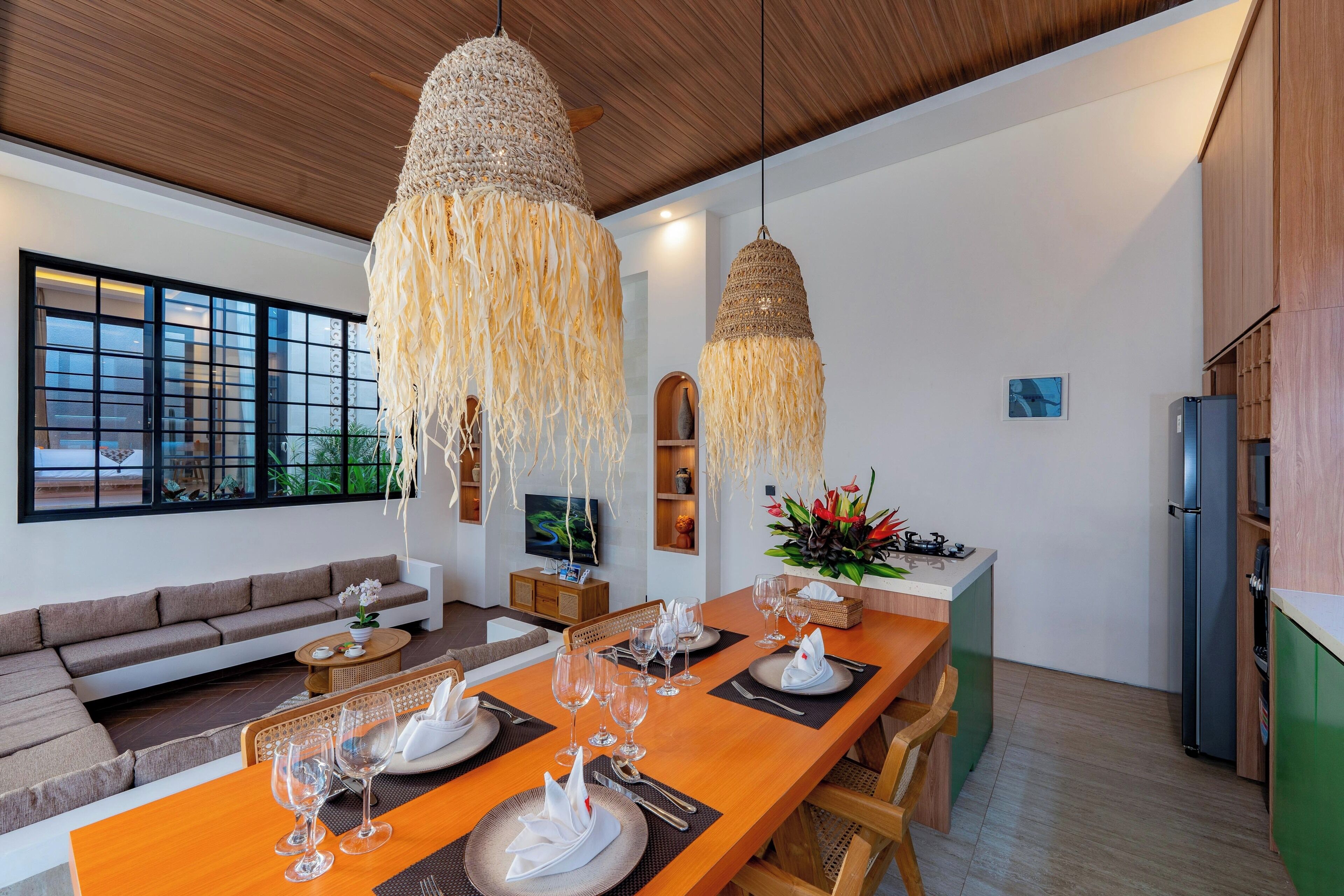 Un comedor moderno con una larga mesa de madera dispuesta para seis personas, rodeada de un acogedor rincón de asientos.
