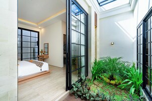Un dormitorio moderno con una cama grande, un escritorio pequeño y vistas de la ciudad a través de amplias ventanas.