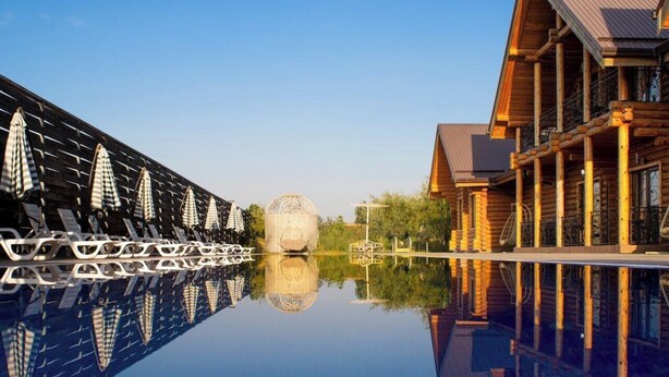 A reflective pool with a wooden building and a row of umbrellas on the left. - GOLDEN FISH GROUP (Urtasaray)