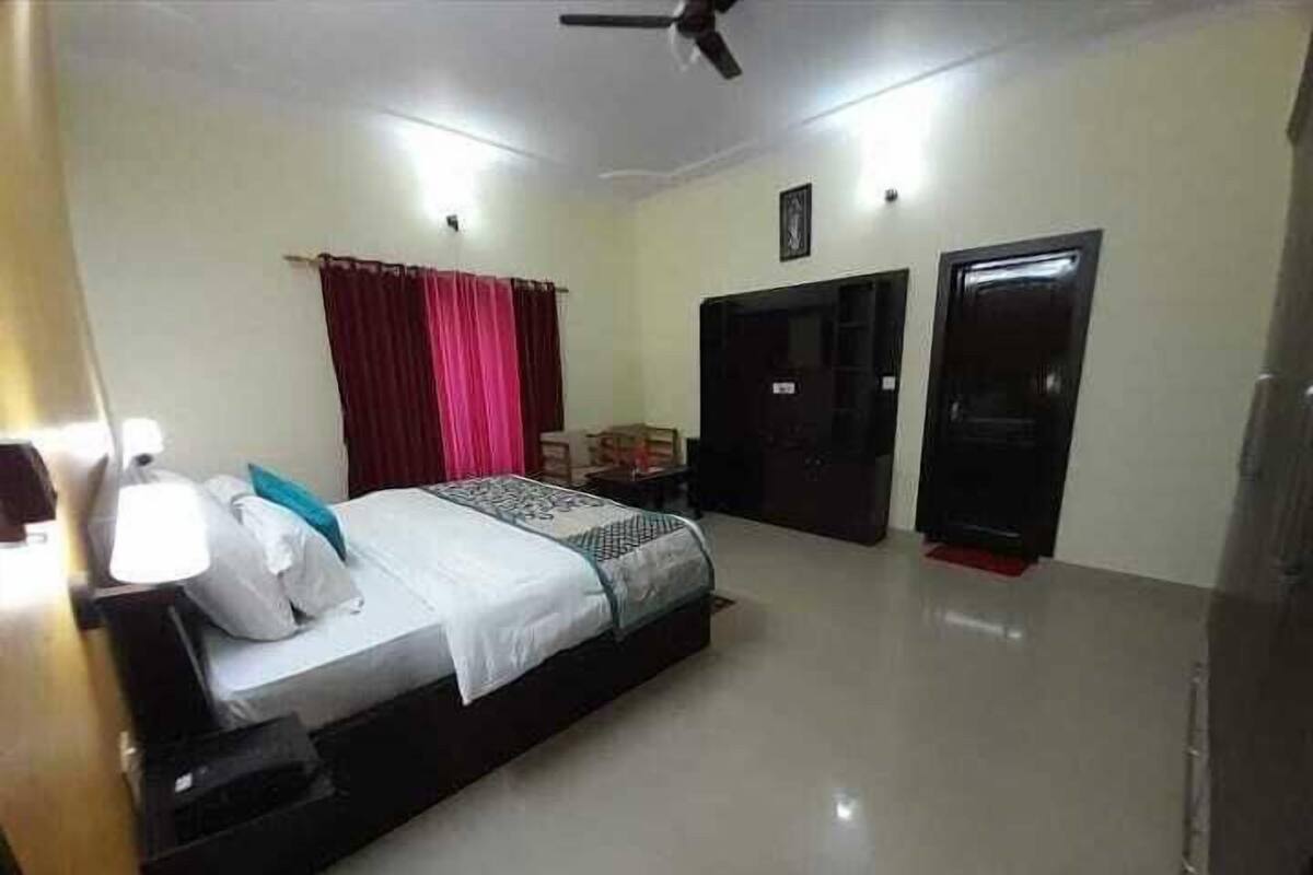 A bedroom with a bed, bedside table, lamp, and curtains.