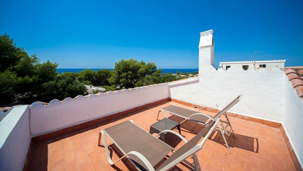 Eine Dachterrasse mit zwei Liegestühlen und einem kleinen Tisch, mit Blick auf einen klaren blauen Himmel und das Meer.