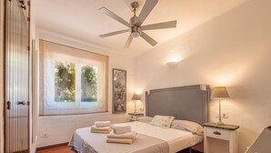 Ein Schlafzimmer mit einem Bett, zwei Nachttischen, einem Deckenventilator, einem Fenster mit Vorhängen und einer Tür.