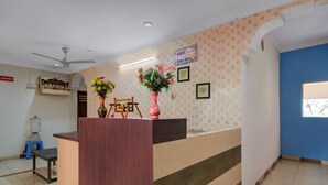 A reception area with a wooden counter, two vases with flowers, a ceiling fan, and a water dispenser. - iROOMZ Hotel Silver Moon (Hyderabad)