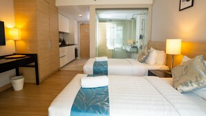 Hotelkamer met twee bedden, een bureau, een kleine kitchenette en een badkamer zichtbaar door een glazen deur.