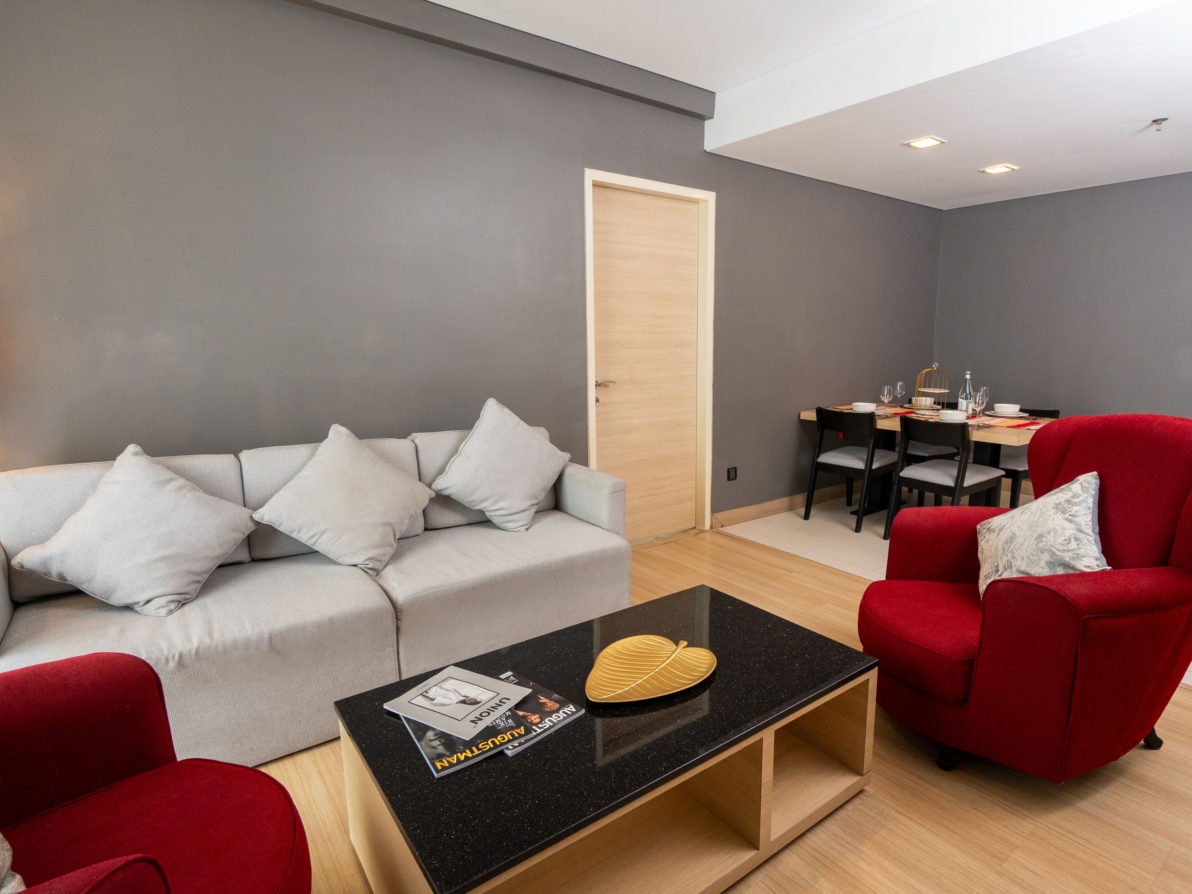 Un salon moderne avec un canapé gris, un fauteuil rouge et une table basse noire sur laquelle sont posés des magazines.