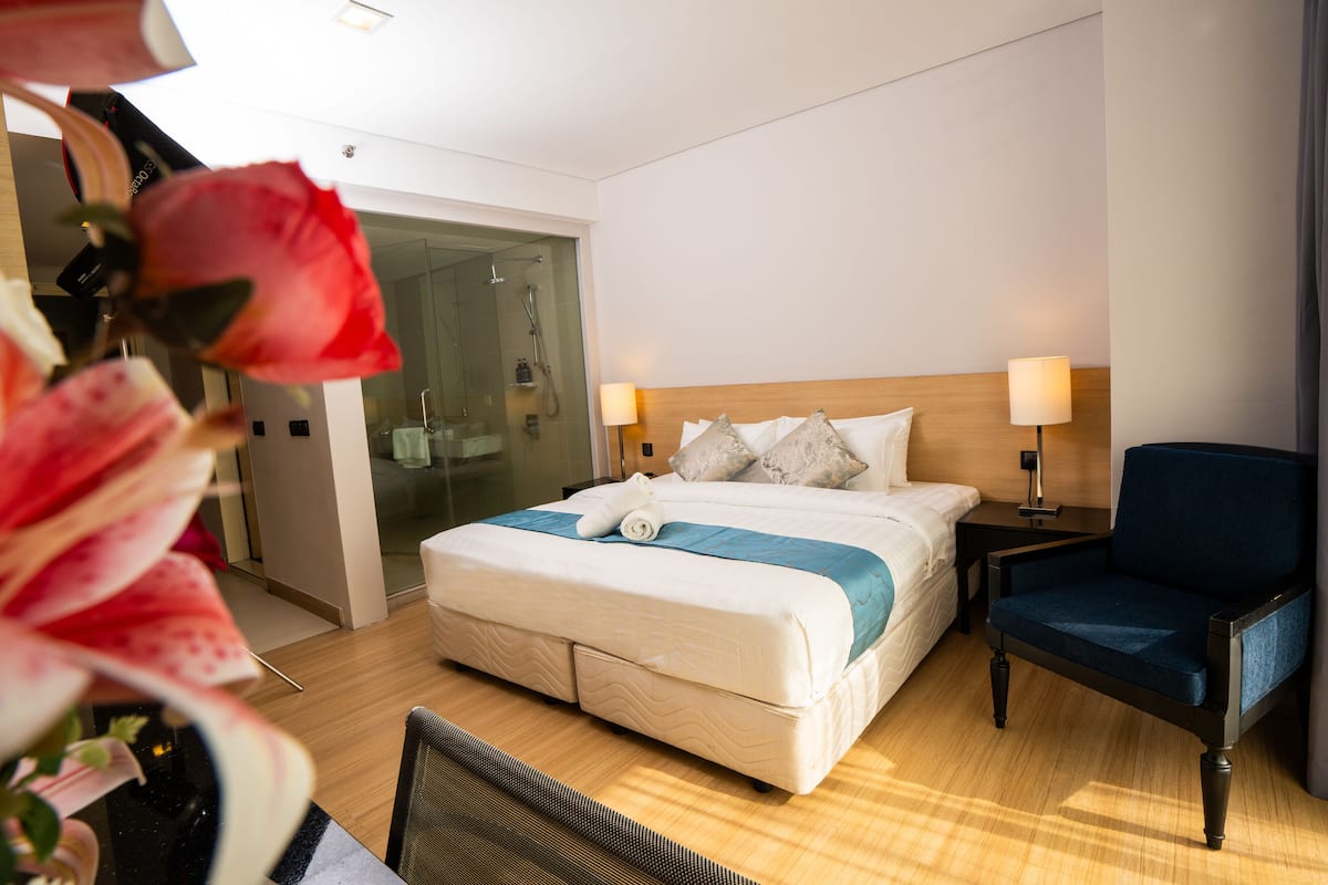 Ein Hotelzimmer mit Bett, Nachttischen, einem Sessel und einer Dusche mit Glasabtrennung.