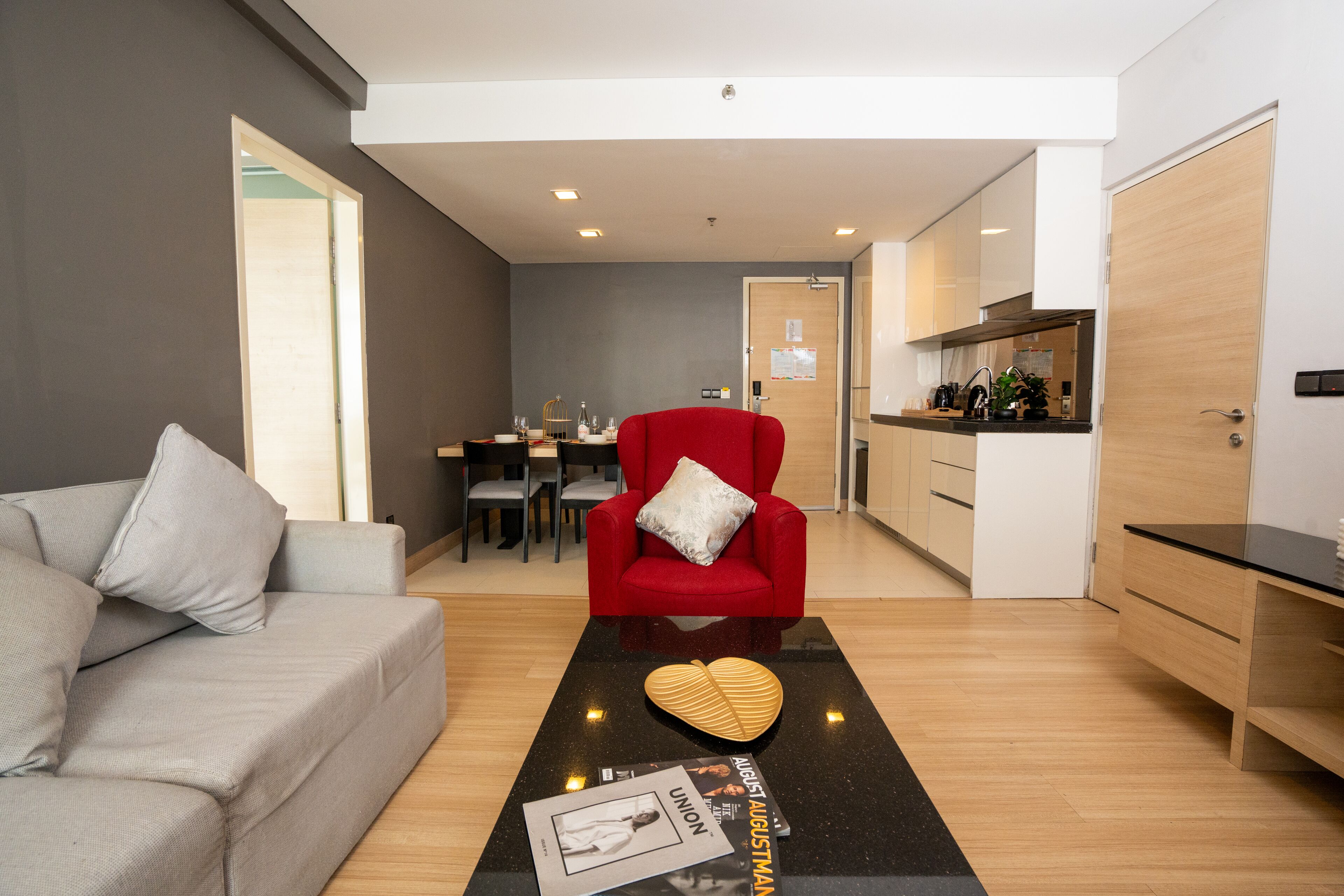 A modern living room with a grey sofa, a red armchair, and a black coffee table with magazines and a heart-shaped object.