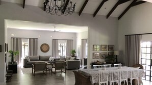 A spacious living room with a high ceiling, a chandelier, a dining table with white chairs, and a sofa set. - Luxury 5 roomed Villa with A/C, swimming pool etc. in Victoria Falls, Zimbabwe (Victoria Falls)