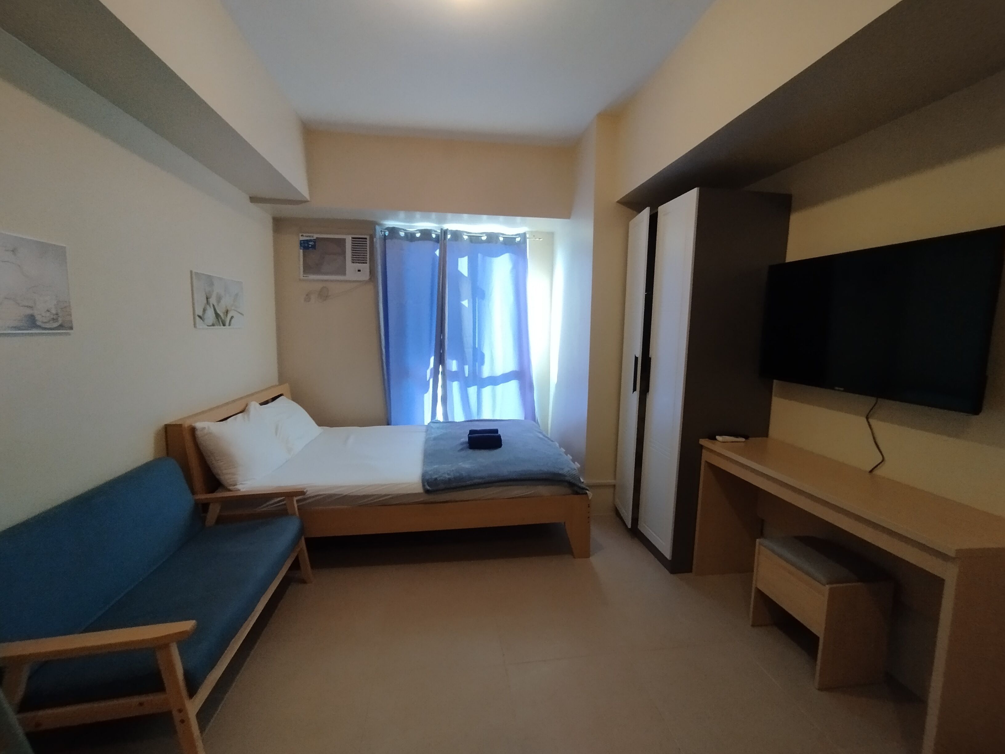 A small, compact room with a bed, a blue sofa, a TV, and a desk.