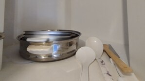 Ein Küchenregal mit einem Edelstahlkochtopf, einem weißen Messlöffel und einem Holzlöffel.