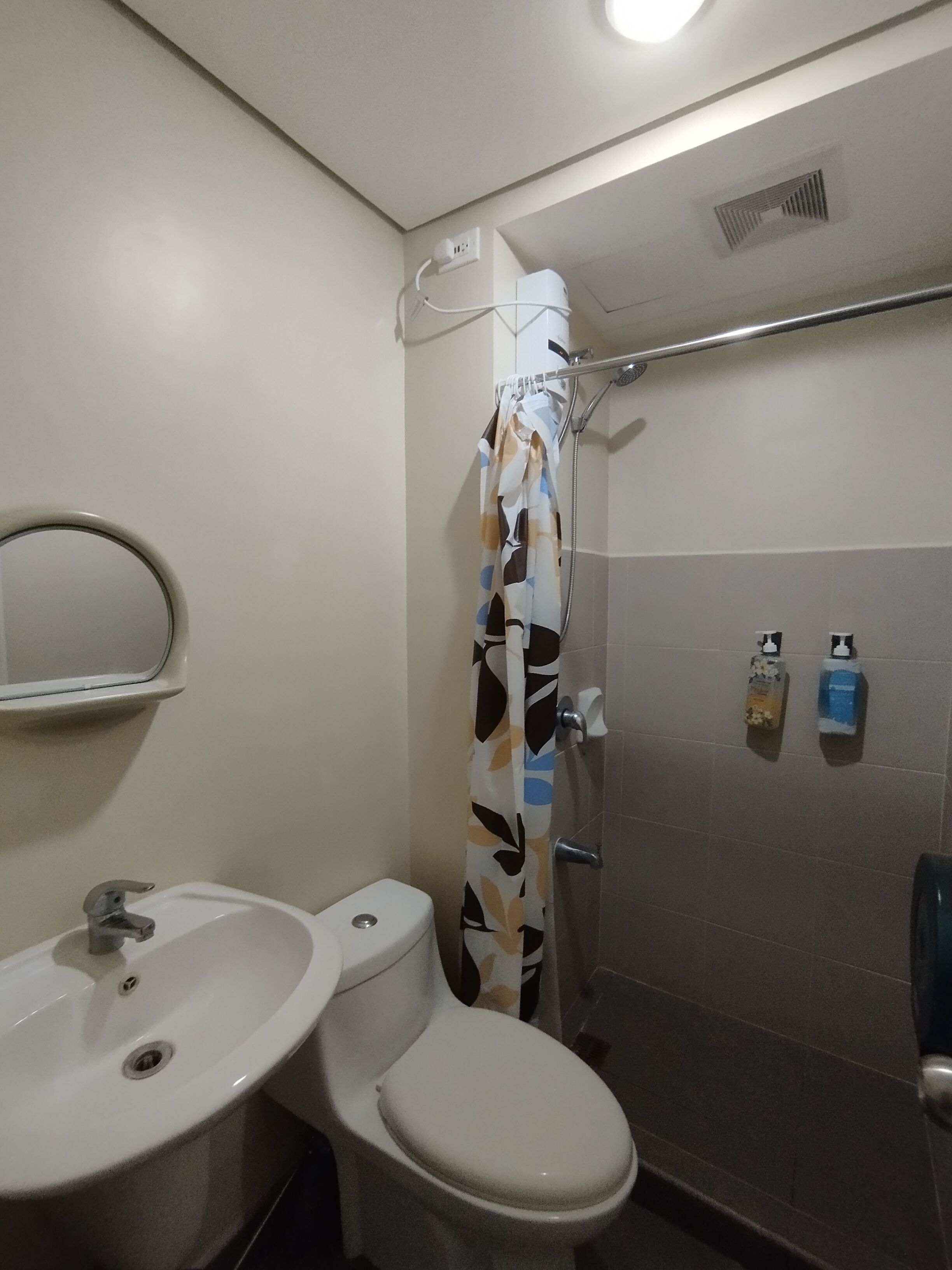 A bathroom with a toilet, sink, shower, and a mirror.