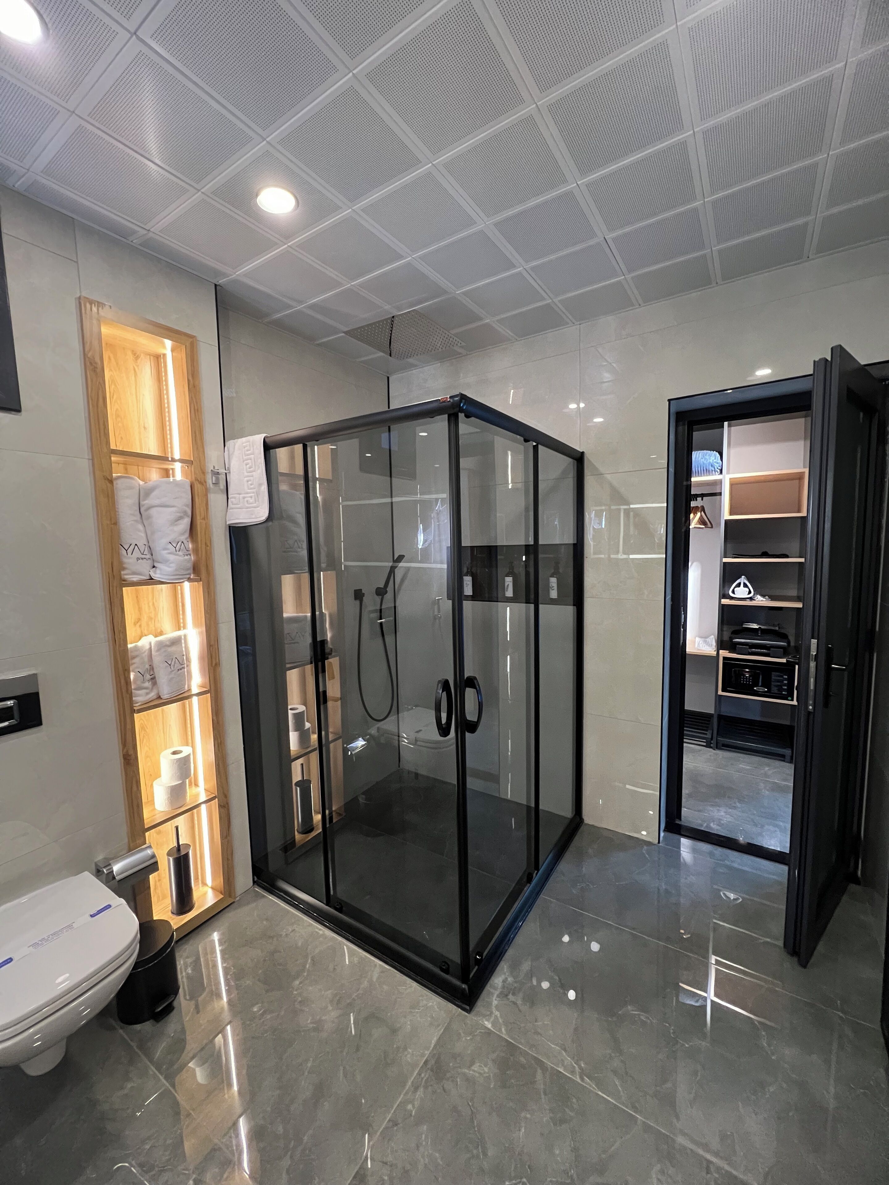A modern bathroom with a glass-enclosed shower, a wooden towel rack, and a toilet.