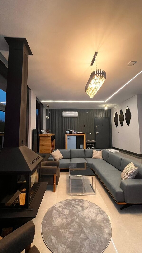 Un salon moderne avec un canapé d’angle, une table basse en verre et une cheminée intégrée.
