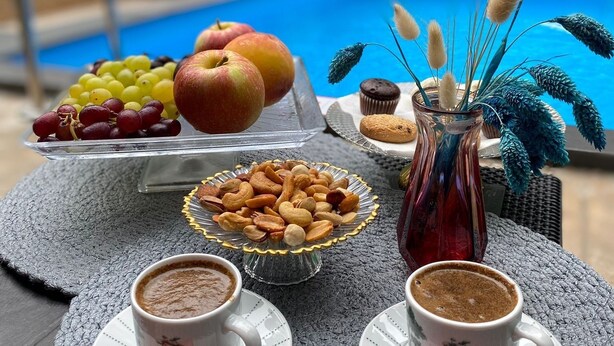 Taula amb menjar i begudes, piscina de fons i una cadira.
