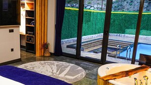 Habitació d'hotel moderna amb un llit gran, una banyera i vistes a una piscina i un jardí.