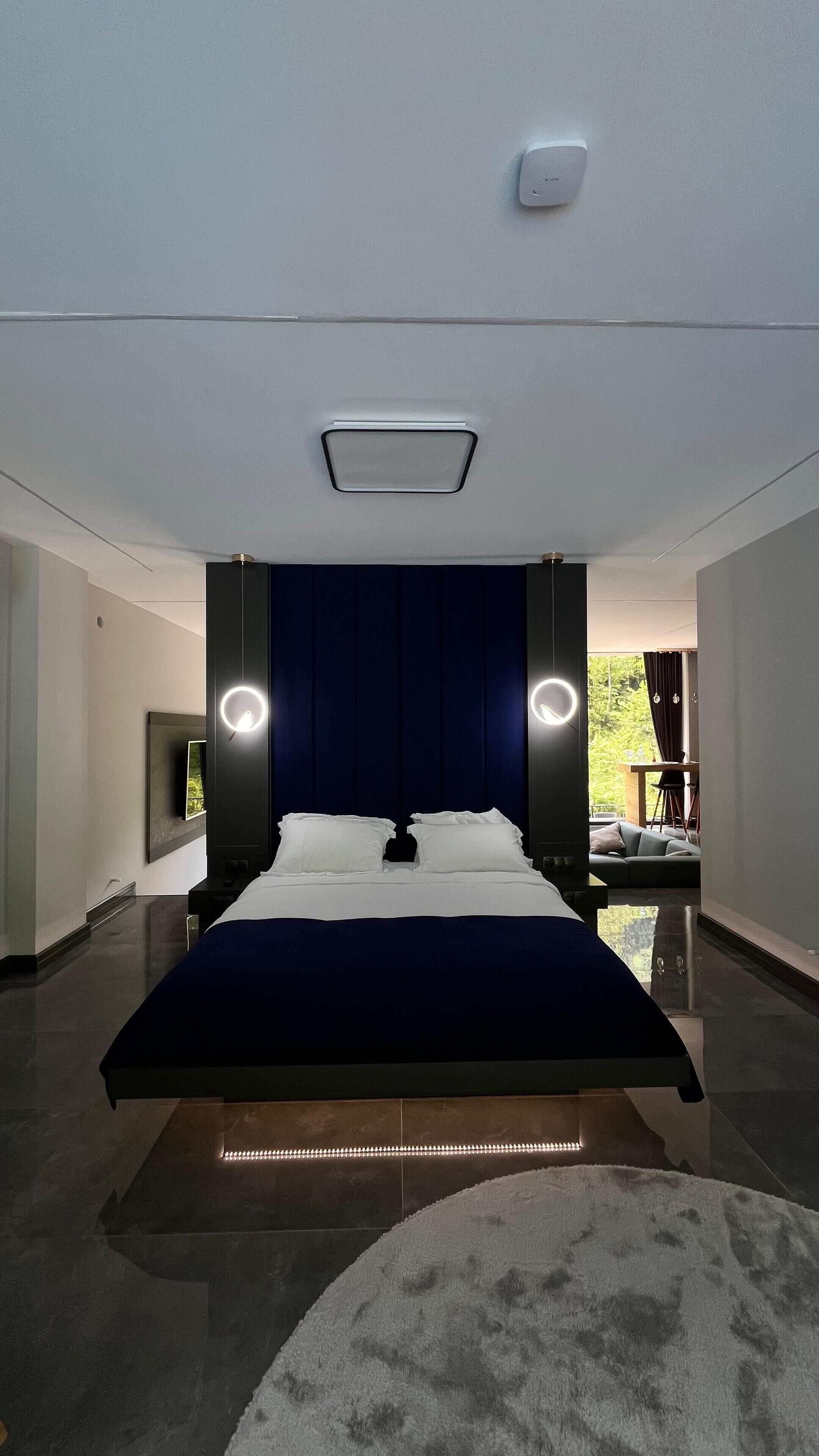 Un dormitorio moderno con una cama grande, dos lámparas de noche, una luz de techo y vistas al exterior.