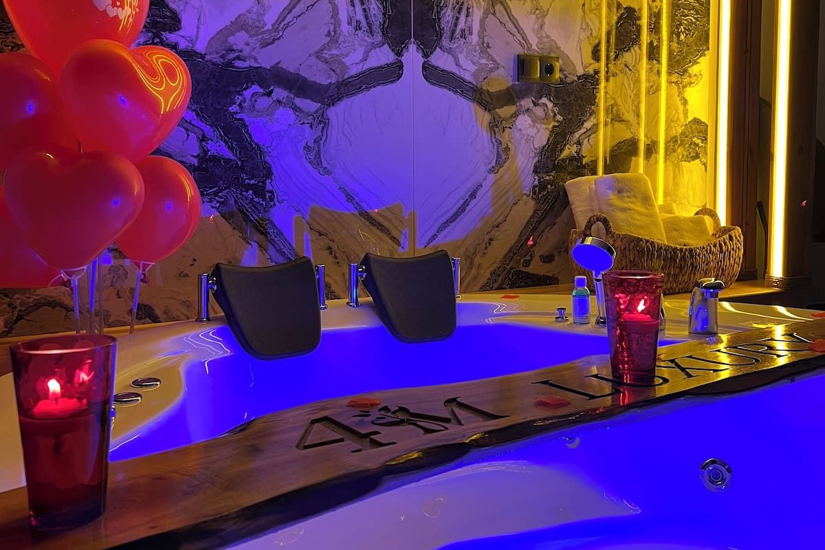 Casa de banho com parede de mármore, banheira com iluminação azul e porta-toalhas.