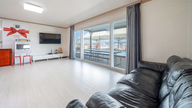 A spacious living room with a large black leather couch, a flat-screen TV, a small entertainment unit, and a view of an outdoor patio with tables and chairs. - Gyeongju Star spa Pension (Gyeongju)