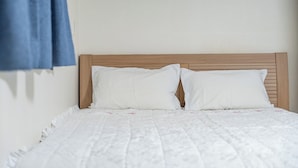 A bed with a wooden headboard, white bedding, and a blue curtain. - Gyeongju Star spa Pension (Gyeongju)