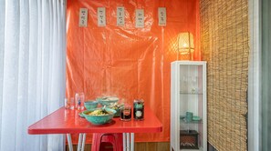Un comedor con una mesa roja, fuentes de comida y un armario con cristalería.