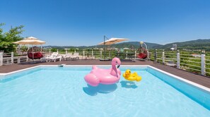 Una piscina con juguetes inflables, sillas de descanso y sombrillas.