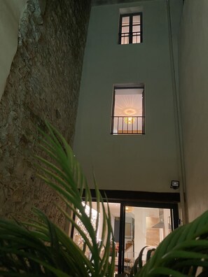 A narrow courtyard with a stone wall on one side and a building with two windows.