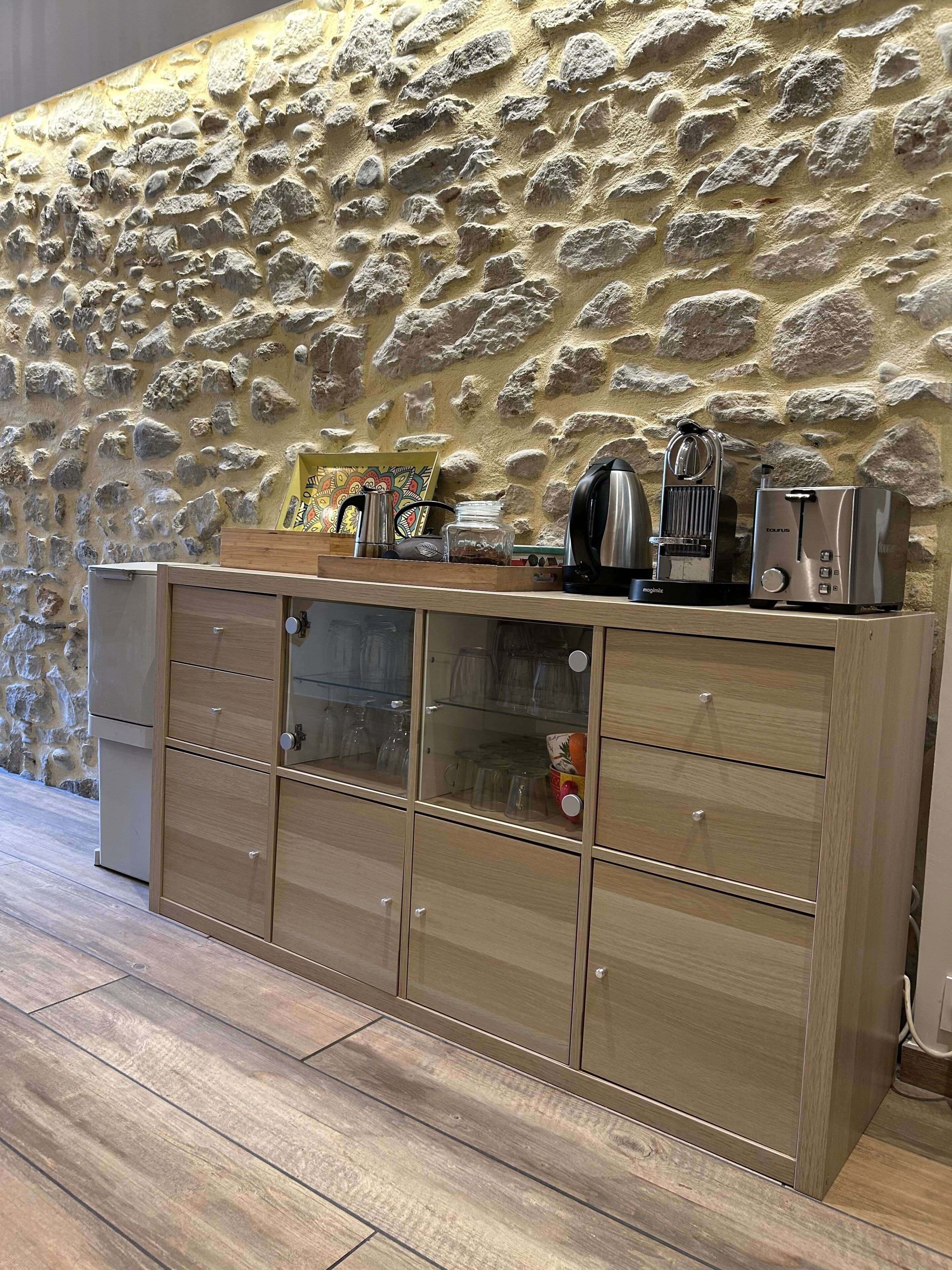 A kitchen with a stone wall, wooden cabinets, and a coffee machine.