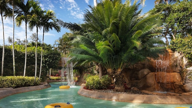 Un parco acquatico con acque cristalline, palme e una cascata rocciosa.