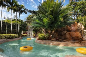 Un parc aquatique avec une eau cristalline, des palmiers et une cascade rocheuse.