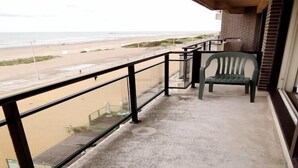 A balcony with a view of the beach, a green chair, and a concrete floor. - Apartment in Nieuwpoort near the Beach (Nieuwpoort)